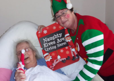 Loose Valley staff member with a bed bound resident and a cheeky Christmas elf