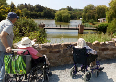 Residents in wheelchairs looking out at a beautiful lake at Hawkhurst Fish Farm
