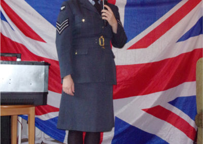A female singer, dressed in an Airforce uniform, singing in front of a Union Jack flag
