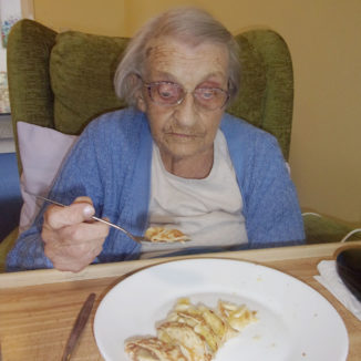 Female resident sat at a table eating a pancake on pancake day