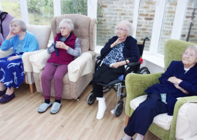 Seated lady residents watching a singer in their conservatory